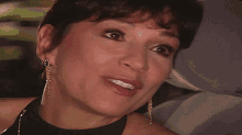 a close up of a woman 's face with a black top and earrings