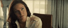 a woman is sitting in a chair in front of a window looking at the camera .
