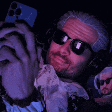 a man with a beard wearing sunglasses and headphones looks at his phone