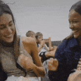 two women are sitting next to each other smiling and laughing in a room .
