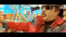 a man wearing sunglasses and a red jacket is holding a gun in front of a ferris wheel .