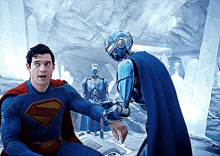 a man in a superman costume is talking to a robot in a cave