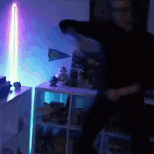 a man is dancing in front of a light saber in a dark room .