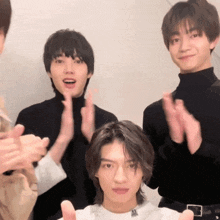 a group of young men are clapping their hands and one of them is wearing a black turtleneck
