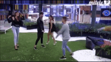 a group of people are dancing on a lawn in front of a building that says mitele