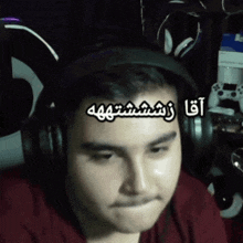 a man wearing headphones and a red shirt has arabic writing on his forehead