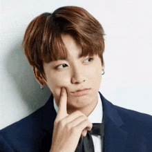 a young man in a suit and bow tie is making a funny face with his finger on his face .