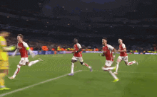 a group of soccer players are running on a field and one of them is wearing a red jersey that says arsenal