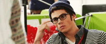 a young man wearing glasses , a beanie and a striped shirt is sitting in a chair .