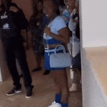 a group of people are standing in a room and a woman is holding a blue purse .