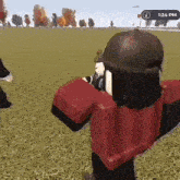 a person in a red shirt and black hat is standing in a field holding a gun .