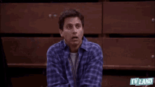 a man in a plaid shirt is raising his arms in the air and making a funny face .