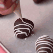 a person is decorating a chocolate ball with white frosting and the word mr.bakes is visible in the corner