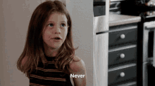 a little girl says " never " in front of a kitchen counter
