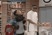 a man and a woman are standing in a store . the man is wearing sunglasses .