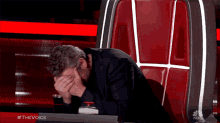 a man sits in a chair with his head in his hands and the words #thevoice on the bottom right