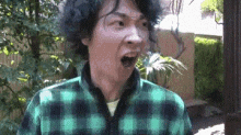 a man with curly hair is wearing a green and black plaid shirt and making a funny face .