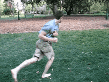 a man in a blue shirt is running barefoot in the grass