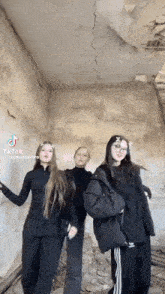 three girls are standing next to each other in a room with a ceiling that is cracked
