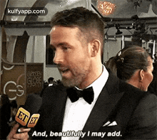 a man in a suit and bow tie is holding a microphone and talking into it .