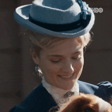 a woman wearing a blue hat is holding a dog and smiling