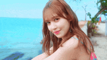 a woman in a bikini is sitting on the beach and smiling at the camera