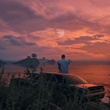 a man standing next to a car looking out over the ocean at sunset