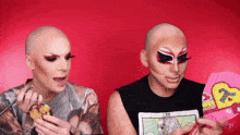 two drag queens are looking at a tarot card with a heart on it