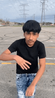 a young man in a black shirt and blue jeans is standing in a parking lot with power lines in the background