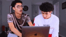 two young men are looking at an apple laptop and one of them is wearing a shirt that says new york