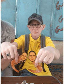 a boy wearing a yellow shirt with two men 's faces on it is holding a shrimp