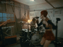 a woman in a red skirt is dancing in front of a drum set in a garage