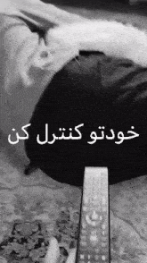 a person laying on a couch holding a remote control with arabic writing on it