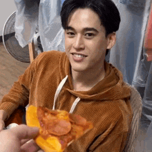 a young man is sitting in a chair eating a slice of pepperoni pizza .