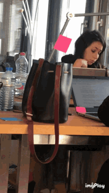 a woman sits at a desk with a laptop and a bottle of water behind her