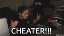 a man is sitting in front of a computer with the words cheater written on the screen