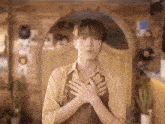 a young man in an apron is holding his hands to his chest in a room .