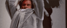 a man with blood on his face is wearing a white shirt and a gray jacket .
