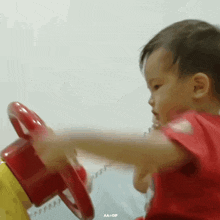 a young boy is playing with a red toy steering wheel .