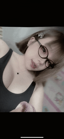 a woman wearing glasses and a black tank top is taking a selfie