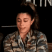 a woman wearing a camouflage shirt is sitting at a table with her eyes closed .