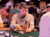 a man is sitting at a poker table in a crowded room playing poker .