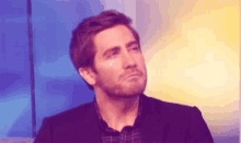 a man with a beard is sitting in front of a blue wall and making a face .
