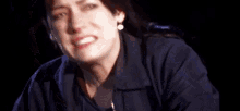 a woman in a blue jacket is making a funny face in a dark room .