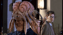 a man in a suit and tie stands next to a monster with a large head
