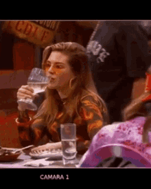 a woman is sitting at a table drinking a glass of wine ..