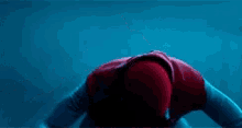 a man in a spiderman costume is kneeling down and pointing at something .