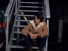 a man in a brown jacket sits on a set of stairs next to another man