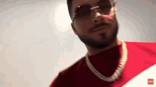 a man with a beard wearing sunglasses and a red shirt is looking at the camera .