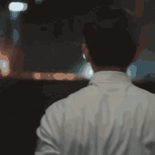 a man wearing a white shirt and a mask is standing in a dark room .